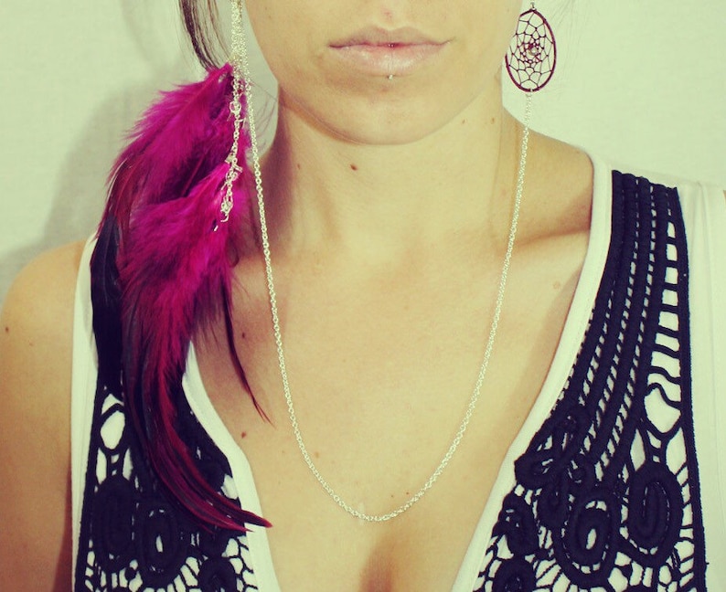 May include: A woman wearing a black and white lace top with a silver chain necklace and a pink feather earring with a silver dreamcatcher charm.