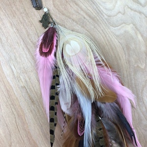 May include: A pink and brown feather hair clip with a gold charm. The clip has a comb on the back for easy attachment.