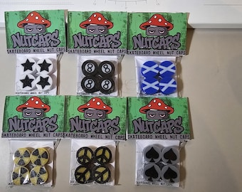 Könnte beinhalten: Verschiedene Skateboard-Radmuttern in transparenten Kunststoffverpackungen. Jede Packung hat einen grünen Header mit einer Pilz-Grafik und dem Text "NUTCAPS". Designs umfassen Sterne, 8-Bälle, blaue Kreuze, gelbe Strahlungssymbole, Friedenszeichen und schwarze Pik.