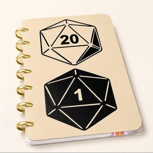 Puede incluir: Un cuaderno de encuadernación de discos en color beige con dos ilustraciones de dados de veinte caras en la portada. El dado superior está delineado en negro con el número 20, mientras que el inferior es negro sólido con el número 1 en blanco.