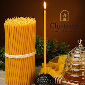 Puede incluir: Una vela amarilla encendida sobre una base negra, con un haz de velas apagadas atadas con hilo a la izquierda. Un tarro de miel de vidrio y un cucharón de miel están en primer plano. El texto "Closterra LIGHT OF SERENITY" es visible.