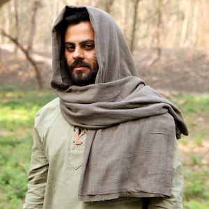 Könnte beinhalten: Eine Person trägt einen grauen Kapuzenschal und eine hellgrüne Tunika. Der Schal ist um den Hals und über dem Kopf drapiert. Die Tunika hat einen V-Ausschnitt mit Lederschnüren.