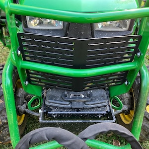 May include: Close-up of a green and black tractor. The tractor has a green roll bar and a black grill. The tires are black with yellow rims. The tractor is on a grassy surface.