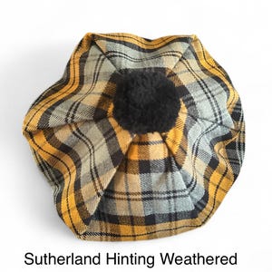 May include: A plaid beret in yellow, black, and gray, with a black pom-pom on top. The beret features a Sutherland Hinting Weathered pattern. The hat is a stylish accessory.