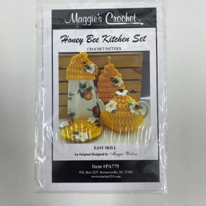 May include: A Maggie's Crochet Honey Bee Kitchen Set pattern package featuring a crochet towel topper, a hanging pot holder, and a tea cozy. The items are yellow with white flower and bee accents. The text reads Honey Bee Kitchen Set, Easy Skill.