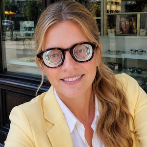 May include: Tortoiseshell-patterned eyeglasses with thick, rounded frames and high-magnification, multi-layered circular lenses. The eyewear features a distinct concentric ring design within the lens area, set against a light-colored frame structure.