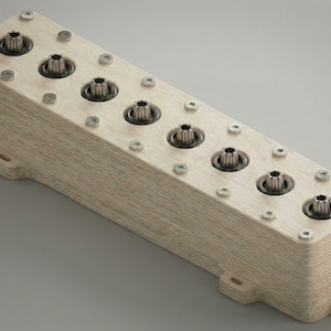 Può includere: Un blocco di legno rettangolare con sei componenti metallici distanziati. Il legno chiaro mostra la venatura, e piccole viti fissano i pezzi metallici. Il design è industriale, con aperture centrali.