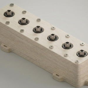 Op de afbeelding: Een rechthoekig houten blok met vijf metalen componenten en meerdere schroeven. Het blok is licht van kleur en heeft een gelaagde textuur. De metalen componenten zijn cirkelvormig met een tandwielachtig ontwerp.