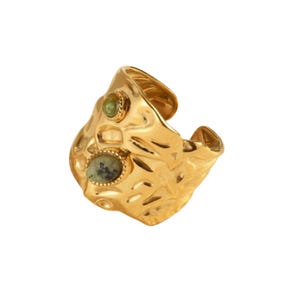 May include: A gold-coloured cuff ring with a textured surface and two green gemstones. The ring has an open design and a hammered metal appearance, showcasing a unique, organic style. The gemstones are oval and round.