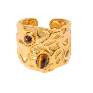 May include: A gold-coloured adjustable ring with a textured surface and two oval-shaped tiger's eye stones. The ring has a hammered metal design and a small round tiger's eye stone.