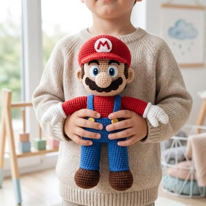 May include: A handcrafted crochet doll of the character Mario, featuring a red cap with a white M emblem, a red shirt, blue overalls with yellow buttons, white gloves, and brown shoes. The doll is made with detailed yarn stitching.