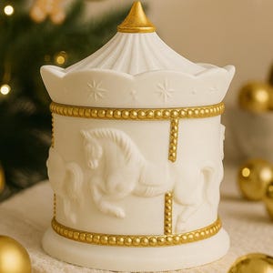 Op de afbeelding: Een witte keramische decoratieve pot met carrouselthema en gouden accenten. De pot heeft reliëf carrouselpaarden en sterdetails. De deksel is conisch met een gouden top. Gouden kralenrand en verticale accenten voegen details toe.