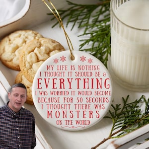May include: A white ceramic Christmas ornament with red text that reads "MY LIFE IS NOTHING I THOUGHT IT SHOULD BE & EVERYTHING...MONSTERS ON THE WORLD." The ornament is next to cookies and a glass of milk.