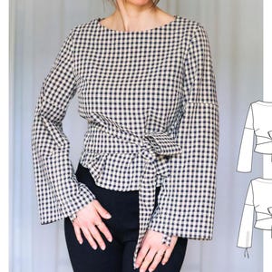 May include: A black and white gingham print blouse with long, flared sleeves and a tie-waist detail. The top has a round neckline and is paired with black pants. A line drawing of the blouse is shown on the right.
