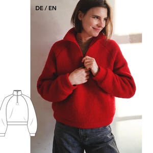 May include: A bright red long-sleeve pullover jumper featuring a high collar with a central zip closure, raglan sleeves, and ribbed cuffs. The garment has a textured, fleece-like appearance and is shown alongside a technical line drawing.
