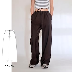 May include: Dark brown wide-leg pants with a drawstring waist and pockets. The pants are shown on a person. A line drawing of the pants is shown next to the pants. The text "DE / EN" is below the line drawing.