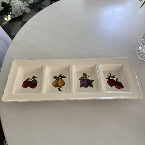 May include: Rectangular off-white serving dish with four square compartments. Each compartment features a different fruit illustration: apples, pears, plums, and pomegranates. The dish has a scalloped edge and a gold trim.