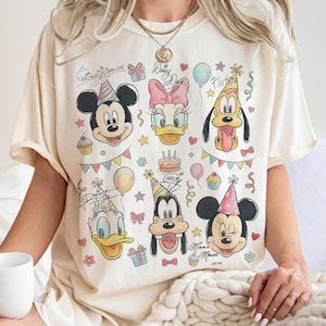 Puede incluir: Camiseta color crema con Mickey Mouse, Daisy Duck, Pluto, Donald Duck, Goofy y Minnie Mouse. El diseño incluye elementos de fiesta de cumpleaños como globos, pastel y confeti. El texto incluye "Mickey Mouse", "Daisy Duck", "Goofy" y "Minnie Mouse".