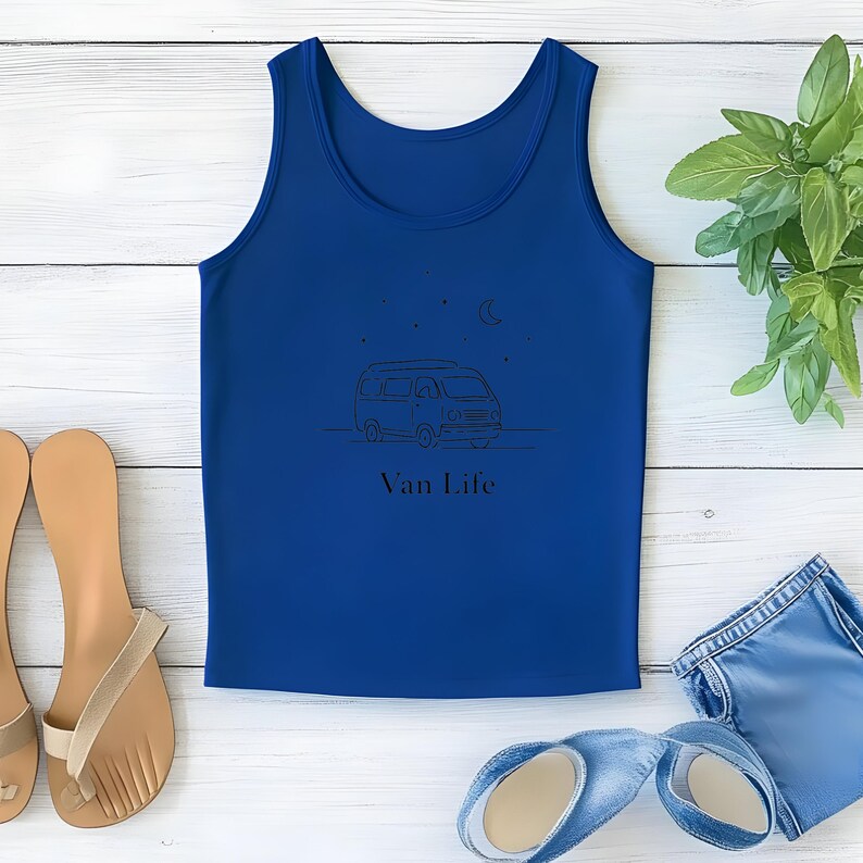 May include: A royal blue tank top with a black line drawing of a van, stars, and a crescent moon. The words "Van Life" are printed below the graphic. The tank top is displayed on a white wooden surface with sandals and denim shorts.