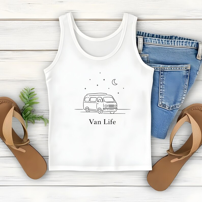 May include: White tank top with a black line drawing of a van, stars, and a crescent moon. The text "Van Life" is below the drawing. The tank top is paired with blue jeans and brown sandals.