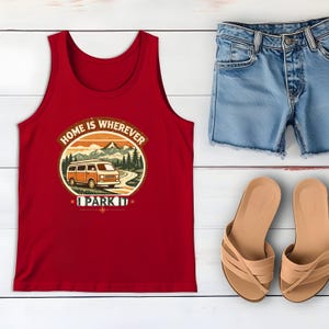 May include: A red tank top with the text "HOME IS WHEREVER I PARK IT" and a graphic of a camper van in a mountain scene. The image also includes denim shorts and tan sandals, all arranged on a white wooden surface.