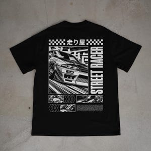 May include: Black t-shirt featuring a white graphic of a sports car and the words "STREET RACER" in a vertical font. The design includes Japanese text and additional car illustrations.
