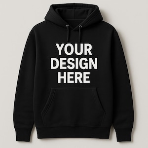 May include: Black hooded sweatshirt with a front pocket and white text reading "YOUR DESIGN HERE". The sweatshirt features a drawstring hood and long sleeves. A classic, comfortable garment for custom designs.