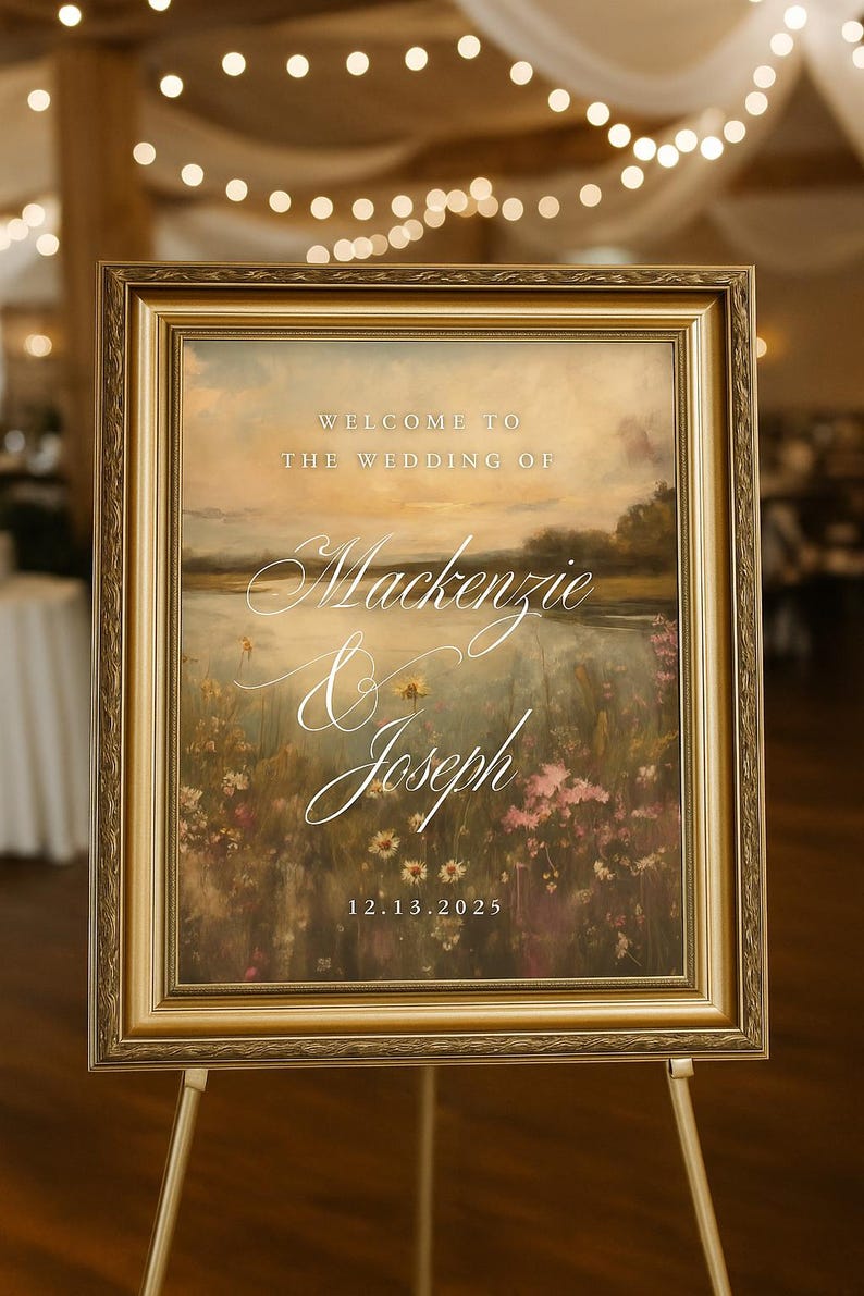 May include: A framed wedding sign with a landscape painting. The sign reads "Welcome to the Wedding of Mackenzie & Joseph 12.13.2025" in elegant script. The frame is gold, and the painting features a field of flowers.