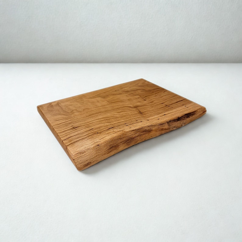 May include: A rectangular wooden cutting board with a natural edge. The board is made of light brown wood with visible grain and texture. The cutting board is approximately 12 inches long and 8 inches wide.