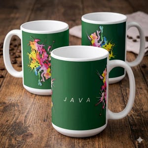 May include: Three white ceramic mugs with a dark green exterior featuring a colorful watercolor paint splatter design. The front-most mug displays the word JAVA in white capital letters centered between the vibrant paint splashes.