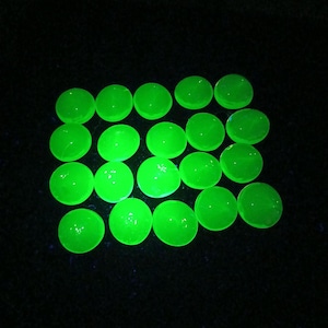 May include: A collection of twenty-one bright green, circular objects arranged on a black surface. The objects appear to be glowing, with a smooth, reflective surface. The overall effect is a vibrant, eye-catching display.
