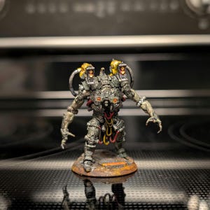 May include: A detailed miniature robot figurine with a metallic gray body, yellow accents, and red and yellow wiring. The robot stands on a circular base with a weathered, rusty appearance. The figure has articulated arms and a complex mechanical design.