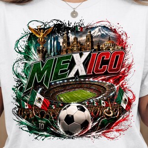 Puede incluir: Una camiseta blanca con un estampado gr&aacute;fico de M&eacute;xico y la palabra MEXICO en letras negritas. El dise&ntilde;o incluye el &Aacute;ngel de la Independencia, un estadio, un bal&oacute;n de f&uacute;tbol y banderas mexicanas, rodeado de salpicaduras de pintura verde y roja.