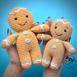 May include: Two crocheted gingerbread men dolls. The dolls are tan with white and light blue accents. They have black eyes and smiles. The dolls have blue buttons and white icing details. The image has the text "PDF PATTERN & INSTRUCTIONS".