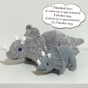May include: Two gray crocheted triceratops toys. The larger plush toy is approximately 13.5 inches long, and the smaller cotton toy is approximately 8 inches long. The toys have white horns and blue eyes.
