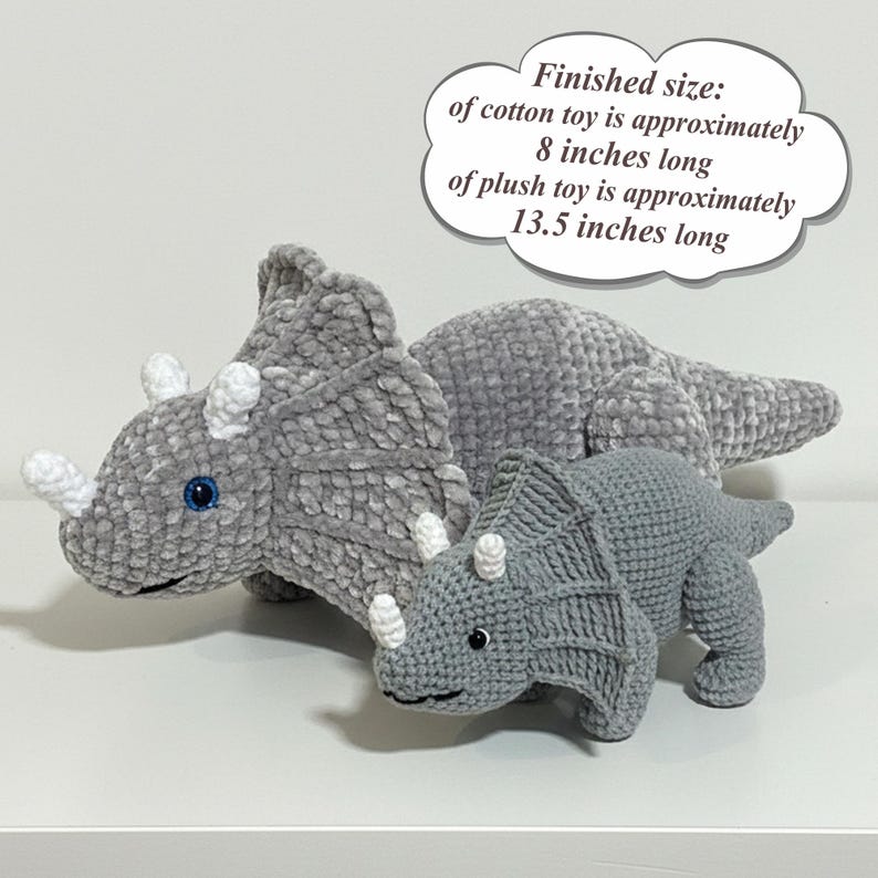 May include: Two gray crocheted triceratops toys. The larger plush toy is approximately 13.5 inches long, and the smaller cotton toy is approximately 8 inches long. The toys have white horns and blue eyes.