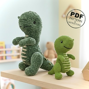 May include: Two green crochet dinosaur toys. The larger dinosaur is standing, and the smaller one is in front. Both have white stripes and smiling faces. The image includes a circular graphic that says "PDF PATTERN & INSTRUCTIONS."