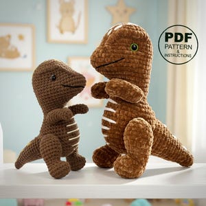 May include: Two brown crocheted dinosaur toys. The larger dinosaur has white stripes and a green eye. The smaller dinosaur has white stripes. The image includes a circular graphic with the text "PDF PATTERN & INSTRUCTIONS".