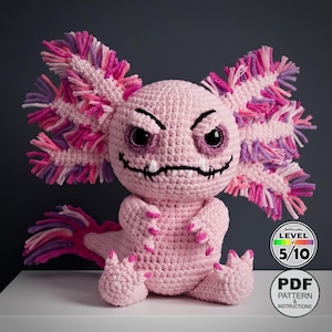 May include: A pink crocheted axolotl with an angry expression. The plush toy has large, dark eyes, a stitched mouth, and fringed gills in shades of pink, purple, and white. The difficulty level is 5/10. The image also includes a PDF pattern and instructions.