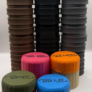 May include: A selection of cylindrical containers in shades of brown, black, and grey, featuring textured sides and flat, labelled tops. The labels read "30-06", "44 MAG", "10mm", and "22 LR".