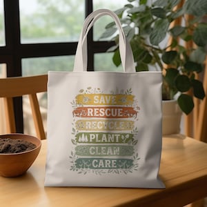 May include: Off-white tote bag with cream-colored handles. The bag features the words "SAVE, RESCUE, RECYCLE, PLANT, CLEAN, CARE" in a colorful, vintage-style design. The bag is sitting on a wooden table.