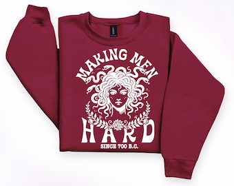 Könnte beinhalten: Burgunderfarbenes Sweatshirt mit weißem Medusa-Motiv und dem Text "MAKING MEN HARD SINCE 700 B.C.". Das Design zeigt eine Medusa-Illustration mit Schlangen als Haare. Das Sweatshirt hat einen Rundhalsausschnitt und lange Ärmel.