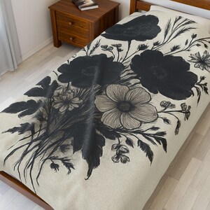 May include: A beige duvet cover featuring a large floral design in black and gray. The design includes large, stylized flowers, leaves, and stems. The duvet is on a wooden bed frame, with a wooden nightstand in the background.