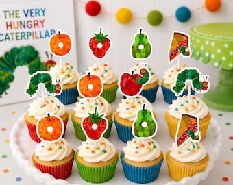 Könnte beinhalten: Eine Sammlung von Cupcakes, die mit Papieraufstellern verziert sind, welche Illustrationen von Früchten und einer Raupe aus The Very Hungry Caterpillar zeigen. Die Cupcakes stecken in bunten Förmchen auf einer weißen, gewellten Platte.