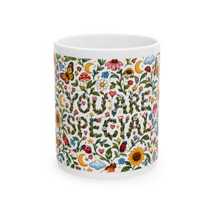 May include: A white ceramic mug featuring a colourful botanical pattern of flowers, butterflies, ladybugs, mushrooms, stars, and crescent moons. The text YOU ARE SPECIAL is printed in the centre in a dark green, leafy, vine-like font.