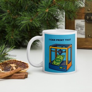 Könnte beinhalten: Weiße Keramiktasse mit dem Text "I CAN PRINT THAT" und einer Cartoon-Illustration eines 3D-Druckers, der einen Geldschein druckt. Die Tasse hat einen blauen Hintergrund und einen weißen Henkel.