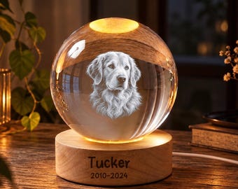 May include: A clear glass sphere featuring a laser-etched portrait of a dog inside, resting on a round wooden base. The base is engraved with the name Tucker and the years 2010-2024, illuminated by a warm light from within the stand.