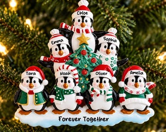 Könnte beinhalten: Ein Weihnachtsbaumschmuck mit sieben Pinguinen, die Wintermützen und Schals tragen. Die Pinguine heißen Chloe, Emma, Sophia, Tara, Noah, Oliver und Amelia. Ein grüner Baum steht in der Mitte und auf der Basis steht der Text Forever Together.