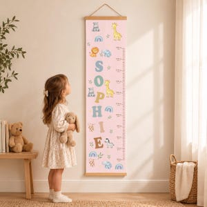 May include: A vertical pink growth chart wall hanging featuring the name SOPHIE in large letters, decorated with illustrations of a giraffe, lion, hippo, elephant, zebra, monkey, and rainbows, with a measurement scale from 80cm to 160cm.