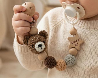 May include: A pacifier clip featuring a cream-colored pacifier, a wooden star bead engraved with the name Evelyn, and a series of round beads in natural wood, dark brown, tan, and gray, along with a crocheted brown bear head accent piece.